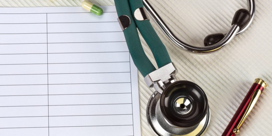 Stethoscope on desk with paper and pen